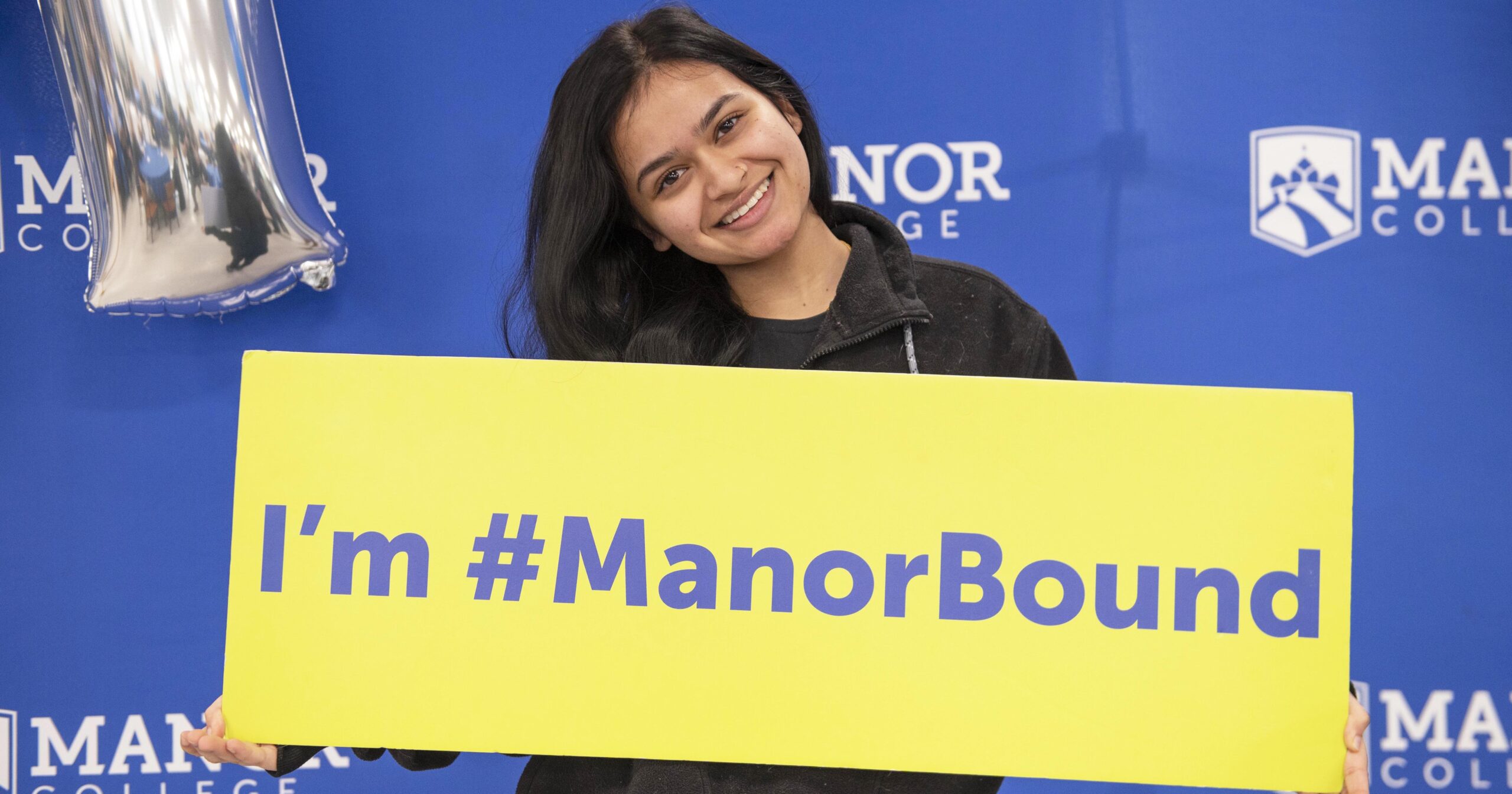 A student holds a sign that says, "I am Manor Bound"