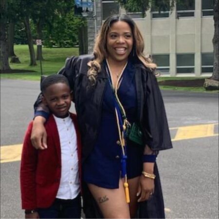 A woman dressed in graduation clothes stands next to her young son.