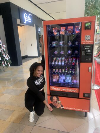 A woman stands next to a vending machine containing hair care products.