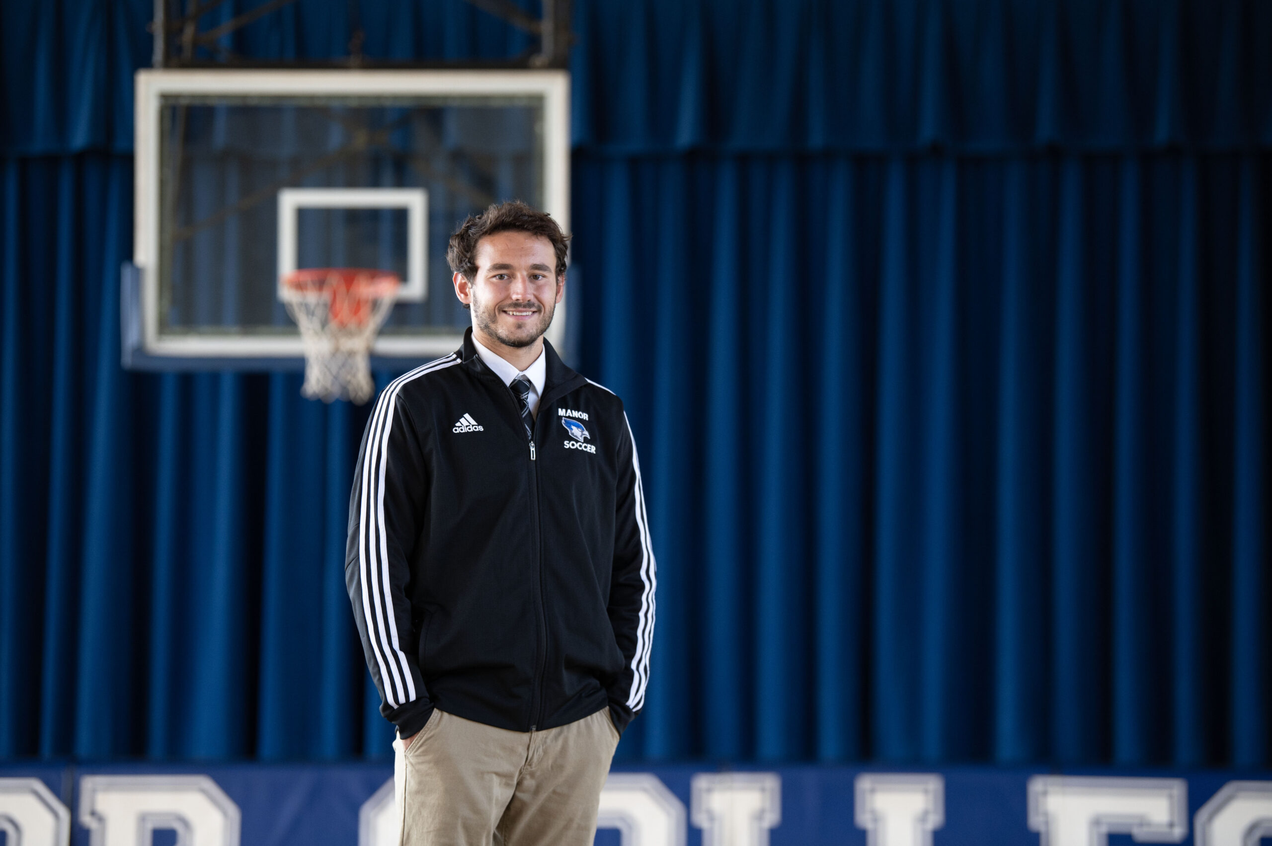 A Manor College student stands in a gymnasium dressed in business attire.