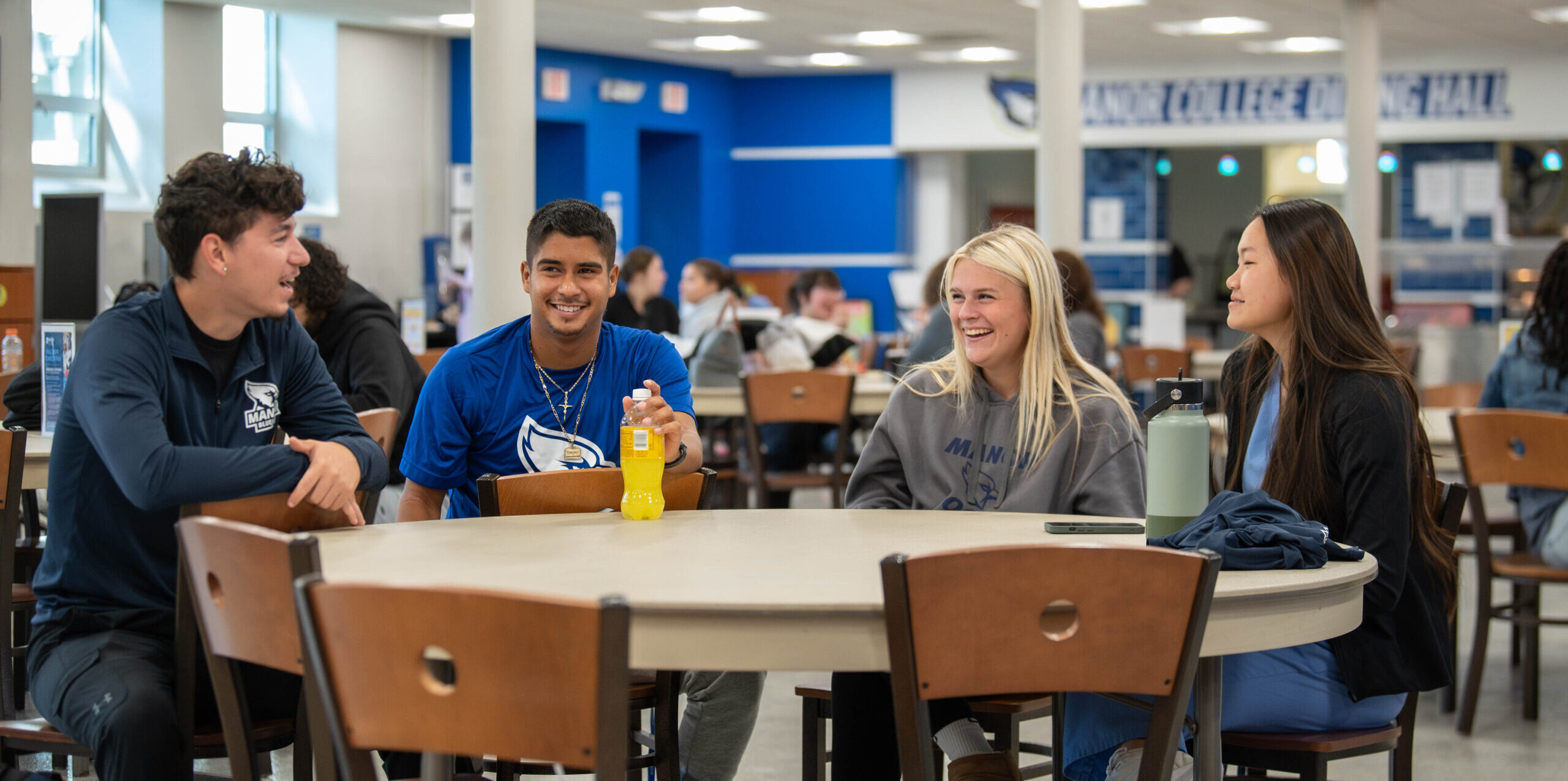 Manor College dining hall with smiling students sitting at a table.